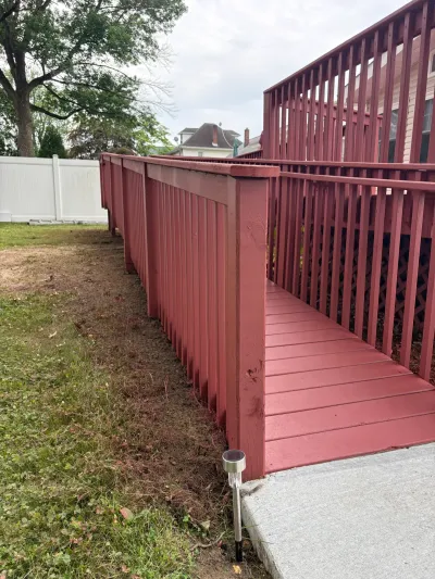 Barn-red painted wood wheelchair ramp with baluster railings running beside a raised backyard deck to a concrete walkway.