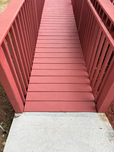 Red painted wooden access ramp with matching railings sloping down to a gray concrete pad.