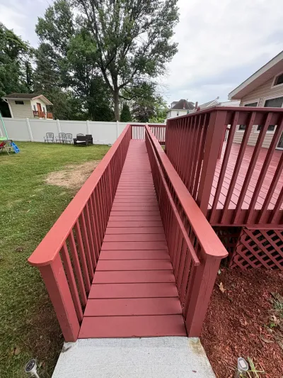 Red-painted wooden accessibility ramp rising from a concrete pad to a raised backyard deck.