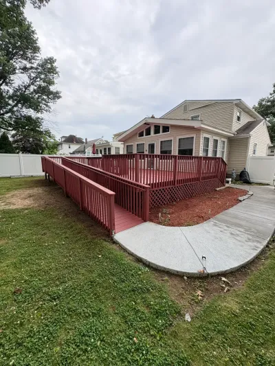 Red-stained backyard deck with a long switchback wheelchair ramp leading to a concrete walkway.