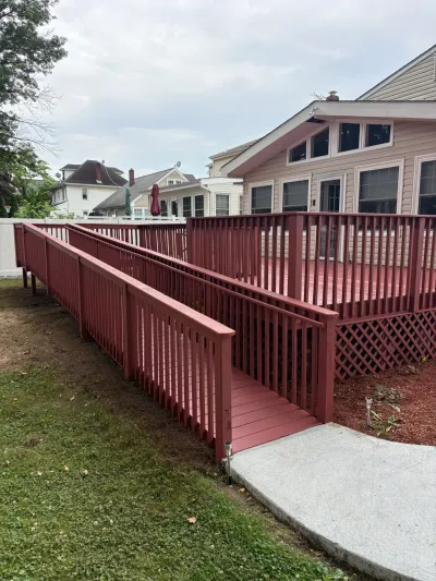 Red-stained backyard deck with picket railing and a switchback wooden accessibility ramp to a concrete walk.