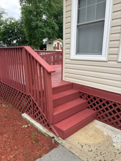 Freshly painted red wood deck with three steps, balusters and lattice skirting beside tan vinyl siding.
