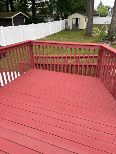 Freshly painted red backyard deck with matching wood railing overlooking a fenced lawn and tan shed.