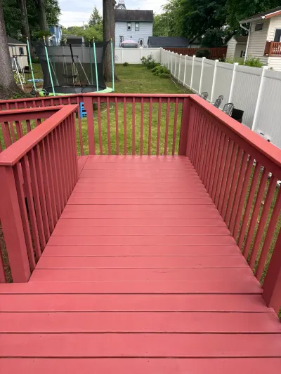 Freshly painted red wood deck with matching railing overlooking a fenced backyard lawn and trampoline.
