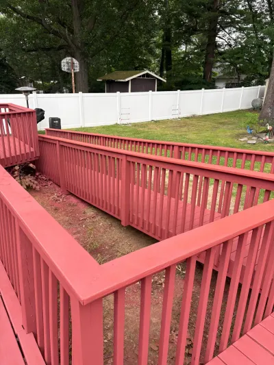 Freshly painted red wood deck with a switchback wheelchair ramp overlooking a fenced backyard.
