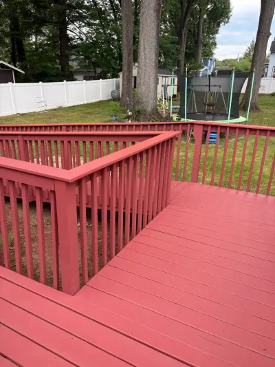 Freshly stained red wood deck with matching baluster railing overlooking a fenced backyard and trampoline.