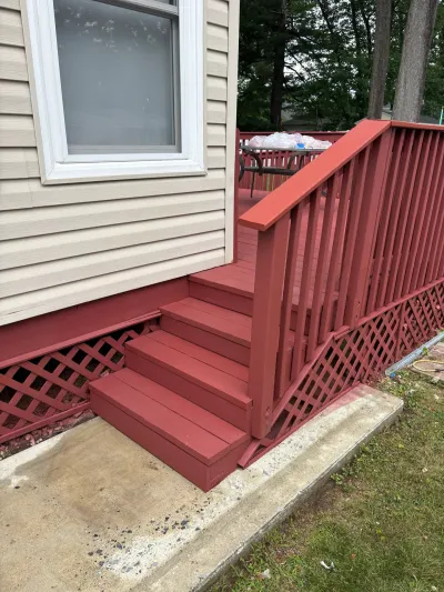 Barn-red painted deck stairs with matching railing and lattice skirting beside tan vinyl siding.