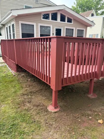 Raised barn-red wood deck with vertical baluster railing attached to a tan sunroom addition