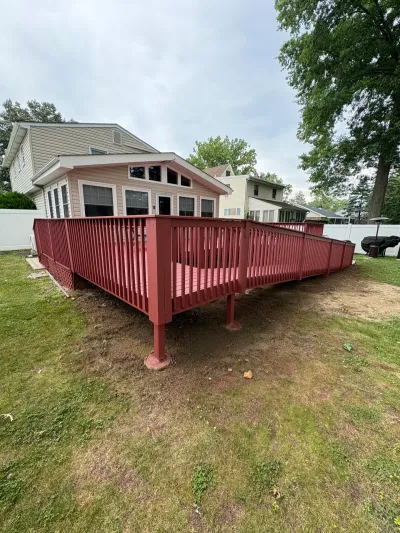 Elevated red-stained wood deck with matching railing attached to the rear of a beige vinyl-sided house.dededeck
