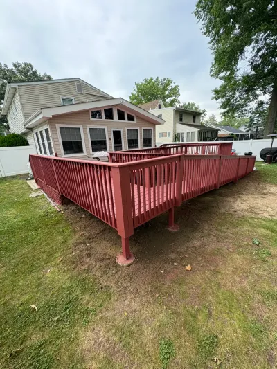 Raised backyard deck stained barn red with picket railings, attached to a tan vinyl-sided house.