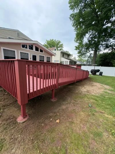 Raised backyard deck painted barn red with matching railing, attached to a tan-sided home.
