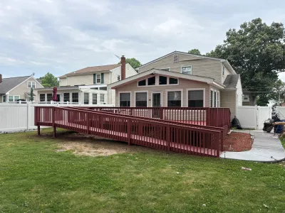 Barn-red stained backyard deck with a long switchback wheelchair ramp against a tan vinyl-sided home.