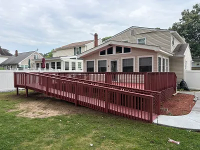 Barn-red wood deck and wheelchair ramp wrapping a tan sunroom addition, with concrete walk and lawn.