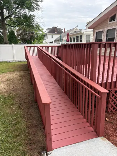 Red-stained wooden wheelchair ramp descending from a raised backyard deck to a concrete pad.
