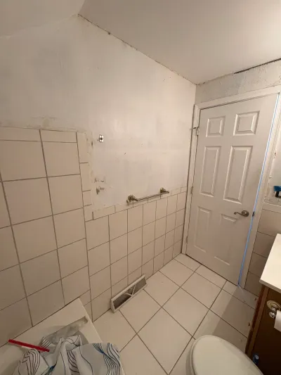 Small bathroom with white tile wainscot, patched drywall, sloped ceiling, and white six-panel door before remodeling.