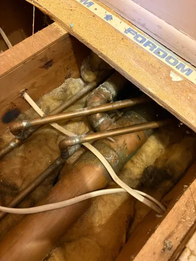 Cut-open subfloor exposing copper pipes, soldered fittings and fiberglass insulation between floor joists.
