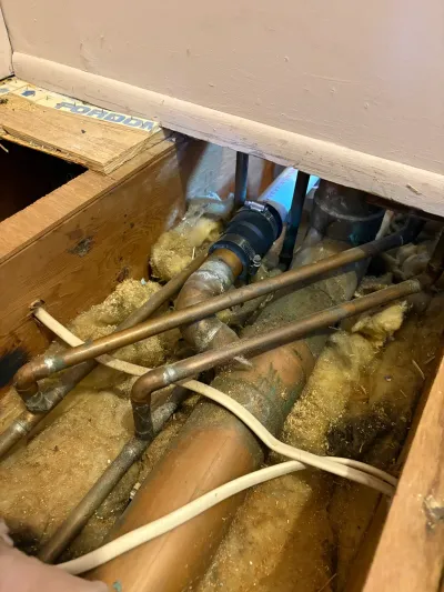 Opened floor cavity showing copper water lines, cast iron drain and insulation between joists