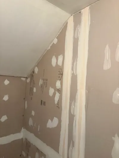 Room corner with taped and mudded drywall and a sloped ceiling, awaiting sanding and paint.