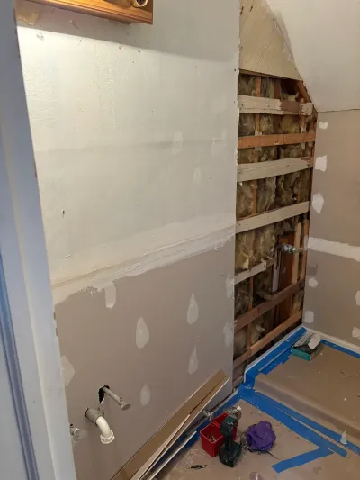 Bathroom mid-renovation with new drywall, an open insulated stud wall, plumbing rough-ins and taped floor.