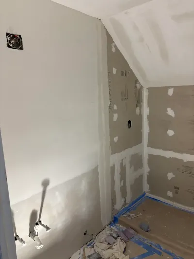 Bathroom under renovation with taped drywall, sloped ceiling, plumbing rough-ins, and protected floor.