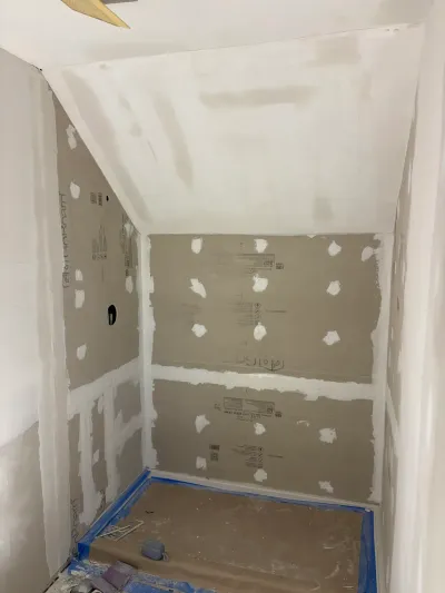 Small bathroom under construction with taped drywall, a sloped ceiling, and paper-protected floor.