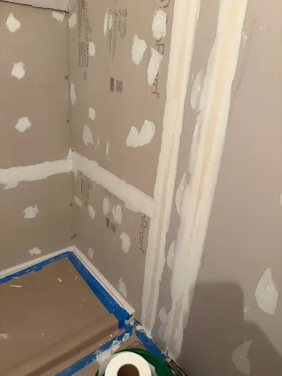 Bathroom corner under construction with taped drywall, tile backer board and paper-covered floor.