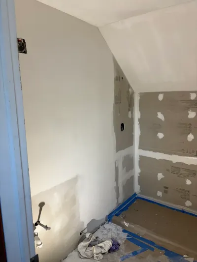 Small bathroom mid-renovation with sloped ceiling, partially mudded drywall and taped paper floor protection.