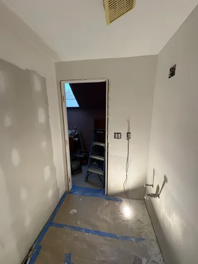 Small bathroom mid-renovation with mudded drywall, paper-covered floor, work light, and capped plumbing stub-outs.