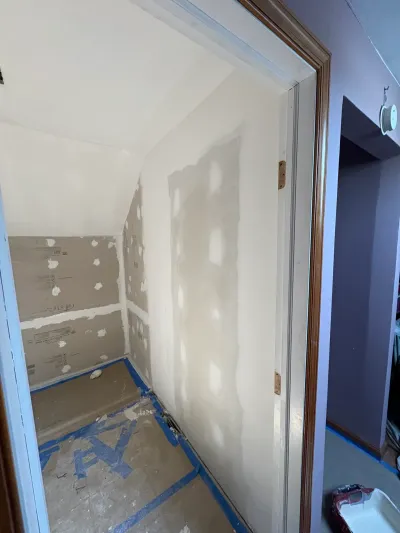 Small closet under a sloped ceiling with freshly taped drywall and taped-off floor protection.