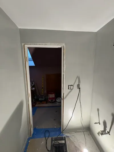 Small bathroom mid-remodel with primed gray sloped ceiling, rough door opening and exposed electrical boxes.