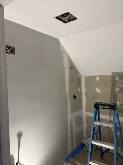 Bathroom mid-remodel with partly primed drywall, sloped ceiling, ceiling fan rough-in and a step ladder.