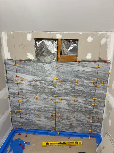 Gray marble-look large-format tile going up a bathroom wall with leveling clips still in the joints