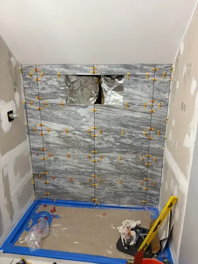 Shower alcove with gray marble-look tile in progress, leveling clips in place and unfinished niche opening.