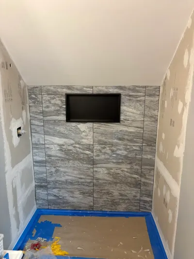 Partially tiled bathroom alcove with gray marble-look porcelain, recessed niche, and sloped ceiling