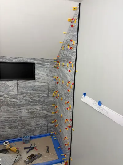 Shower walls mid-installation in gray marble-look porcelain tile with leveling clips and a recessed niche.