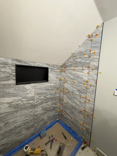 Gray marble-look tile going up in a shower with leveling clips still in place under a sloped ceiling.