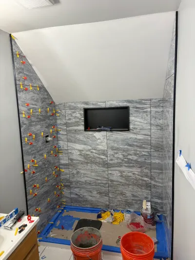 Walk-in shower mid tiling with gray marble-look porcelain, black niche, leveling clips, and sloped ceiling.