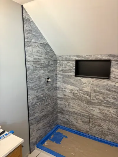 Gray marble-look tiled shower under construction with recessed niche and tile cut to a sloped ceiling.