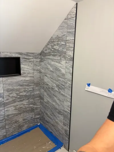 Gray marble-look tile shower under construction beneath a sloped ceiling, with a recessed niche and taped floor.