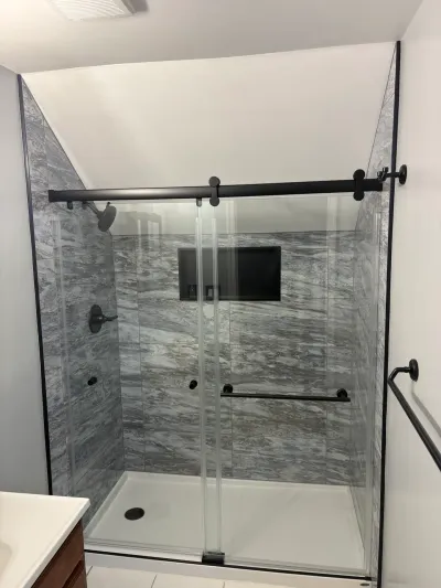 Finished walk-in shower with gray marble-look tile, matte black sliding glass doors, and sloped ceiling.