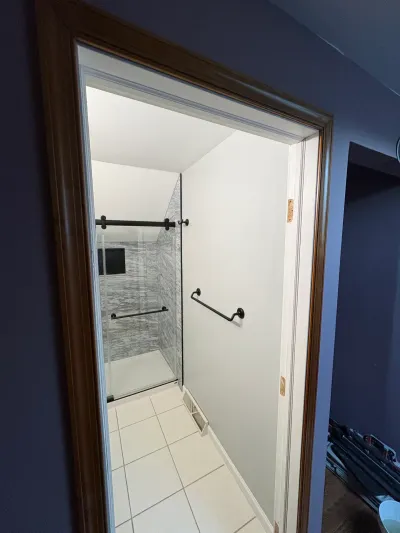 Finished bathroom seen through a doorway, with gray tiled walk-in shower and matte black sliding glass door.