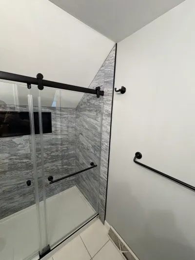 Finished shower with gray marble-look tile, matte black sliding glass doors, and a sloped attic ceiling.