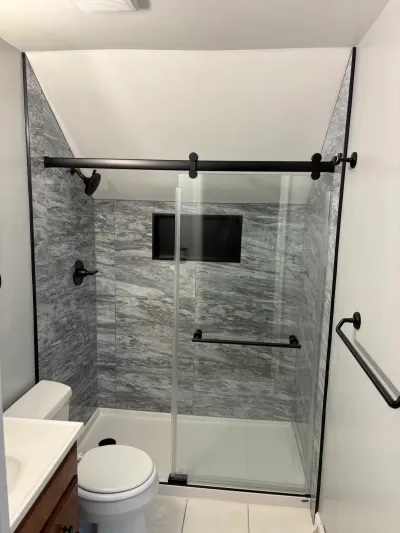 Alcove shower with gray marble-look tile, matte black sliding glass door, and sloped ceiling above.
