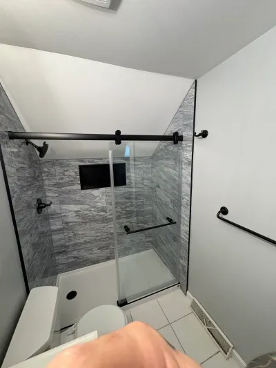 Gray tiled alcove shower with matte black fixtures and sliding glass door under a sloped ceiling.
