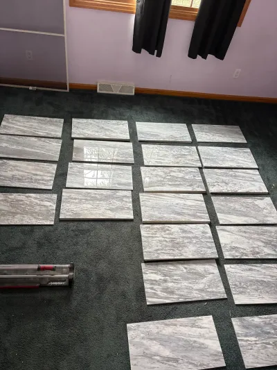 Gray marble-look porcelain tiles dry-laid in rows on green carpet with a manual tile cutter nearby.