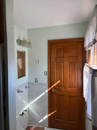 Small bathroom before remodel with green walls, white tile wainscot, wood panel door, and removed medicine cabinet.