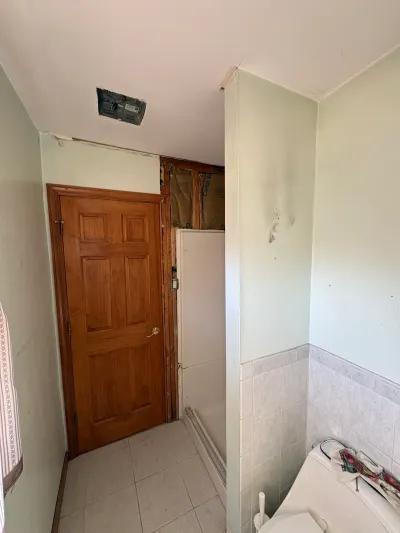 Dated bathroom before remodeling, with green walls, white tile wainscot, wood door, and an open ceiling fan housing.