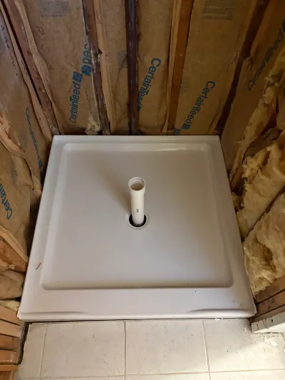 White square shower base set in a corner alcove framed with exposed studs and insulation during a bathroom remodel.