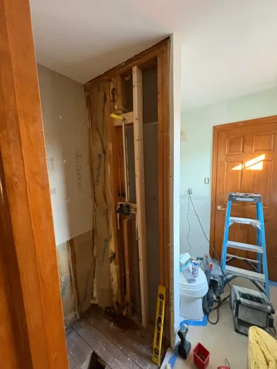 Bathroom mid-remodel with shower wall stripped to studs, insulation and backer board exposed, tools nearby.