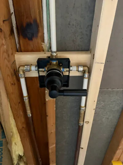 Shower valve rough-in with brass fittings and PEX lines mounted in an open stud wall during construction.
